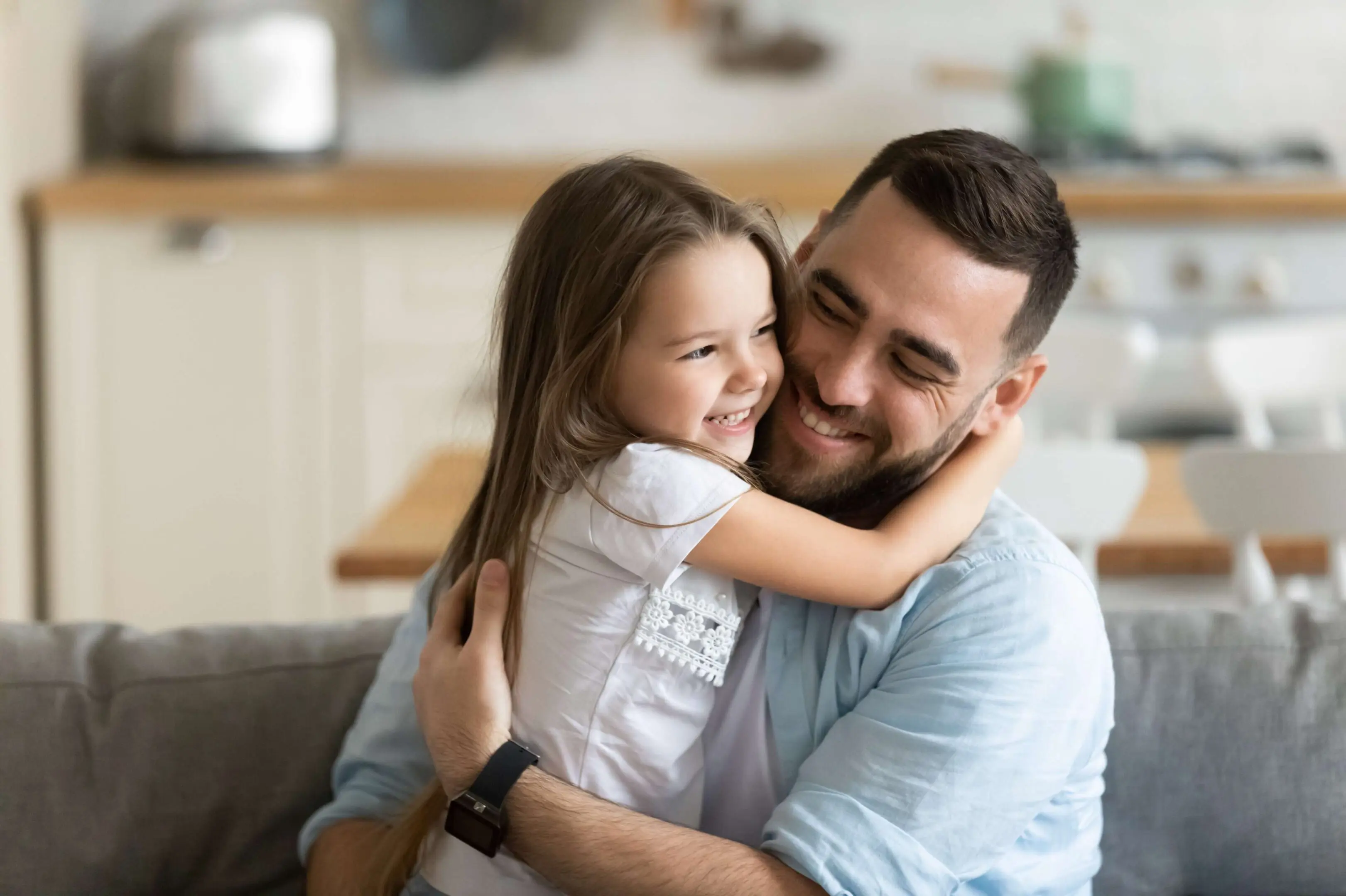 Father and daughter hugging on couch, smiling.